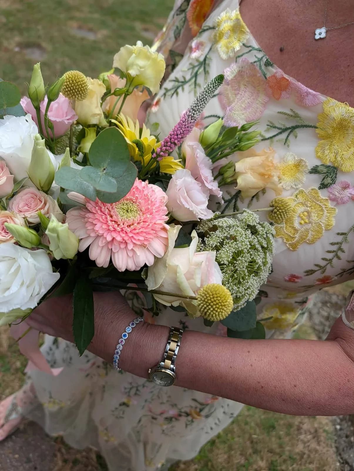 A pastel bridal bouquet held against a floral embroidered dress